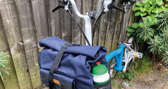 A utility bag hangs at the front of a Brompton bike, the foldable commuter-style bicycle