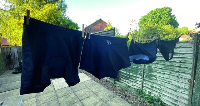 Four pairs of black padded cycling pants hang on a washing line in a garden