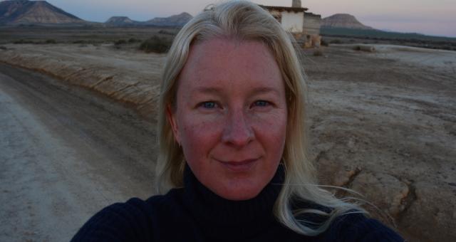 Close-up headshot of Anna in a desert landscape. She is wearing a dark jumper.