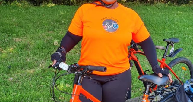 Joscelyne smiling with her red bike. She is wearing an orange Sara Park CCC t-shirt, black leggings and helmet.