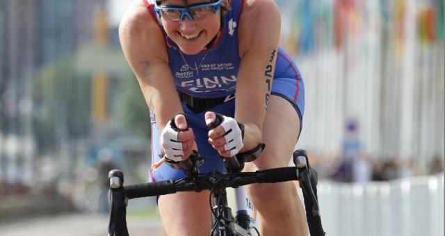 Kath competing in a road bike event. She is wearing a white helmet and blue lycra kit.
