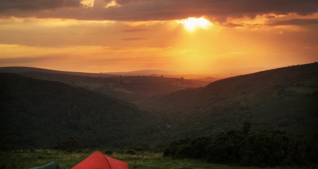Small red tent pitched on a hill at sunset