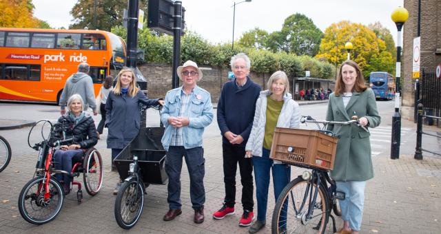 A mixture of men and woman stand with Roxanne. One woman is sat in a recumbent, one is stood next to a cargo bike, and Roxanne stands with a Dutch-style bicycle sporting a basket on the front