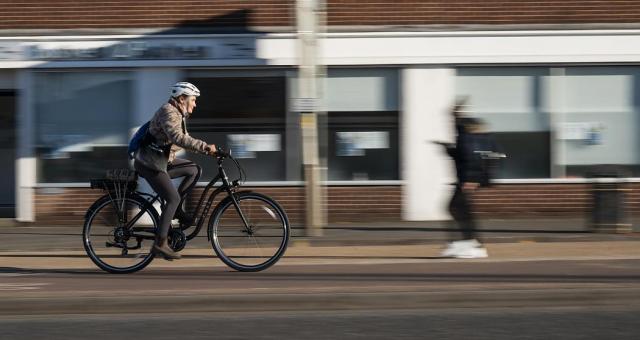 A woman wearing white helmet and purple leggings whizzes along on an e-cycle, background blurred