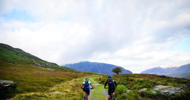 A man and a woman cycle along a rocky path along a Welsh mountain range