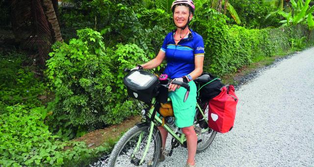 A woman stands over an adventure bicycle which is loaded with pannier bags. She is wearing a helmet and casual summer clothes