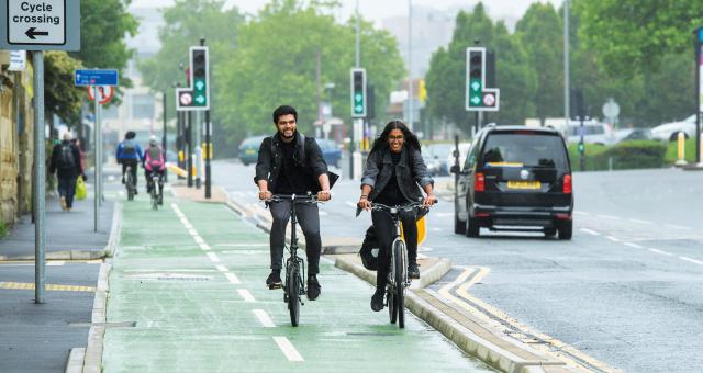 A male and female cyclist ride down a segregated cycle lane next to a busy road
