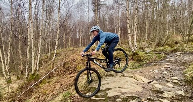 A women wearing a grey helmet, blue jacket and trousers rides a mountain bike downhill in Scotland