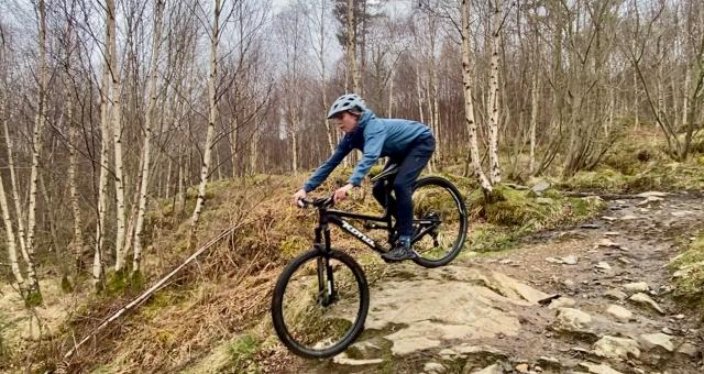 A women wearing a grey helmet, blue jacket and trousers rides a mountain bike downhill in Scotland