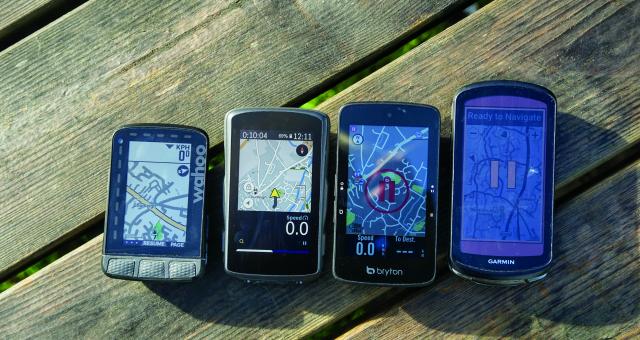 Four GPS bicycle computers are laid in order of size on a picnic bench, each of them displaying a map view.