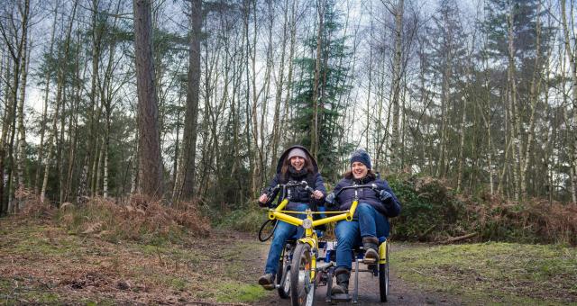 two women riding a twinbike tandem in the forest