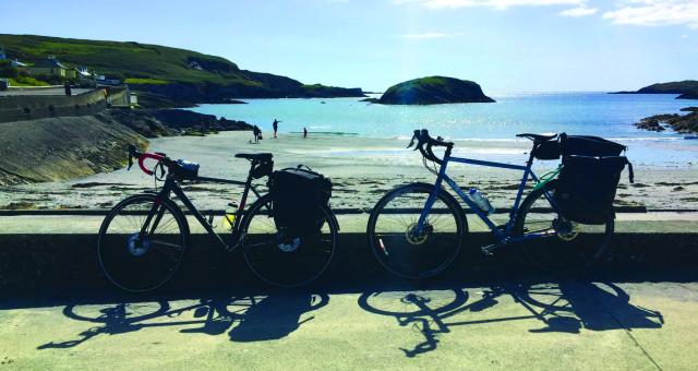 Two bicycles are propped up against a low wall in front of a beach and sea view