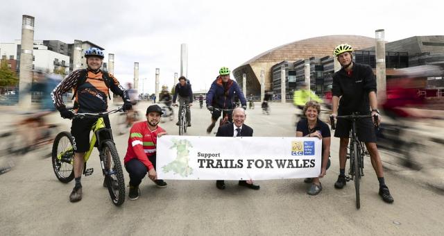 Several people with bikes stand behind a banner reading 'Support Trails for Wales'