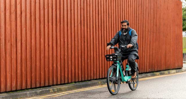 Man pedals electric TIER e-cycle passed wooden wall on road