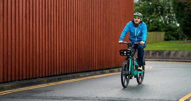 Man wearing helmet and blue jacket smiles as he pedals green TIER e-cycle on road