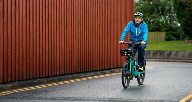 Man wearing helmet and blue jacket smiles as he pedals green TIER e-cycle on road