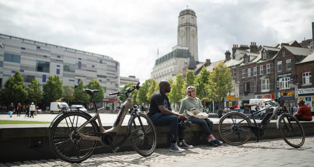 Two people sit next to their e-cycles in Luton city centre on a sunny day