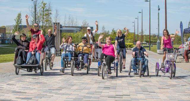 A group of people riding various types of cycles all waving at the camera