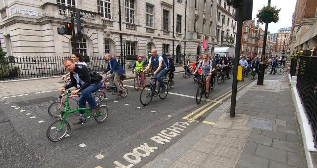 A big group of people are cycling along a London street. There is a mix of bikes and people