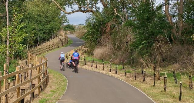 Two people cycle along a wide smooth tarmac cycle path
