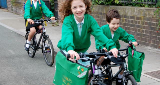 Three young children are cycling along a segregated cycle path. They are all wearing green school uniform