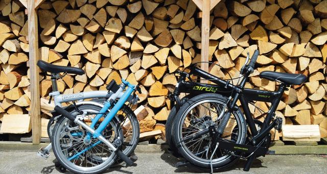 Two folding bikes are folded up in front of a pile of logs