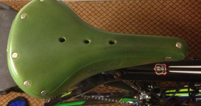 A close-up of a green Brooks saddle on a black bike, taken from above
