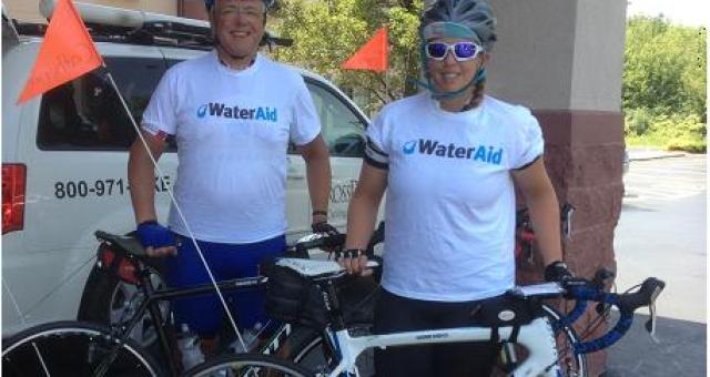 A man and a woman stand behind their bikes. They're wearing WaterAid t-shirts and helmets