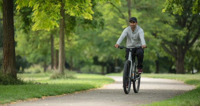 A man wearing a grey cap pedals an e-cycle through a park on a sunny day