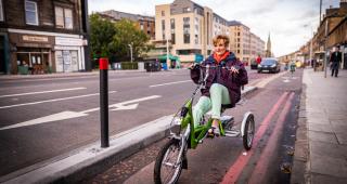A woman rides a trike along a protected cycle lane beside a wide road in Edinburgh