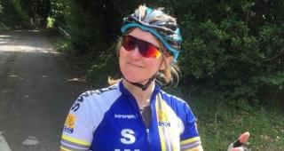 A woman in cycling clothing is smiling and putting her thumb up