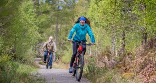 Women off road cycling in the sun on a gravel path, with a man cycling behind