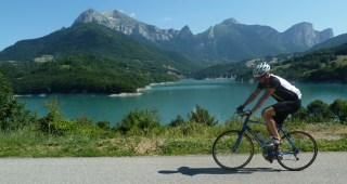 Man cycling on a road with a lake and mountain range in the distance behind him