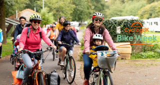 Group of cyclists on a path cycling through a park with two women at the front, one with a small child on the bike too