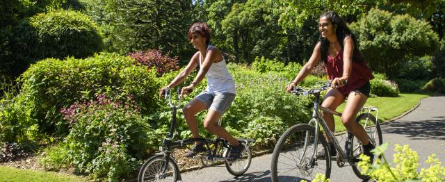 Two women cycling on a path out in the sun © Joolze Dymond