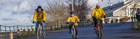 Three individuals cycling together on a road wearing yellow jumpers