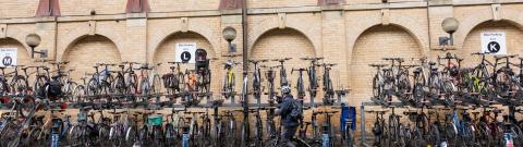 A person is wheeling a bike past several cycle racks with lots of bikes in them at a railway station