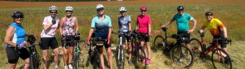 A group of people holding bikes is standing in a field with a blue sky in the background