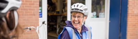 Woman smiling while standing over her bike wearing a helmet