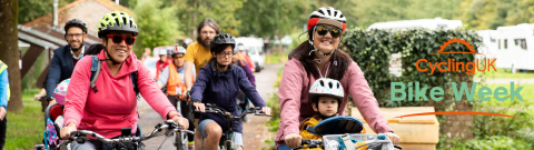 Group of cyclists on a path cycling through a park with two women at the front, one with a small child on the bike too