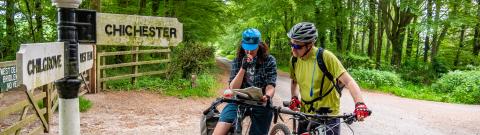 Two Cyclists consulting a map, a road sign next to them pointing in two different dirrections.