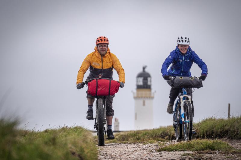 Two bikepackers cycling away from the lighthouse at Cape Wrath. Photo Robby Spanring