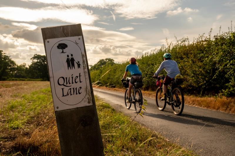 Two people cycle past a 'Quiet Lane' sign on a rural road