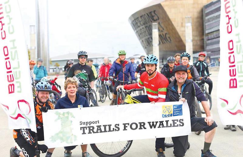 A group of people with bikes are posing with a banner that reads 'Support Trails for Wales'