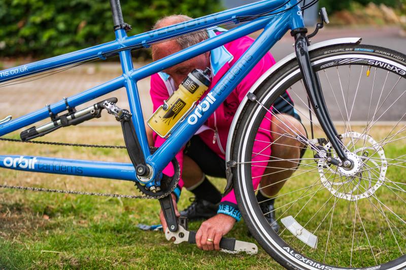 A man in cycling kit is using a spanner to adjust the pedals on a blue tandem