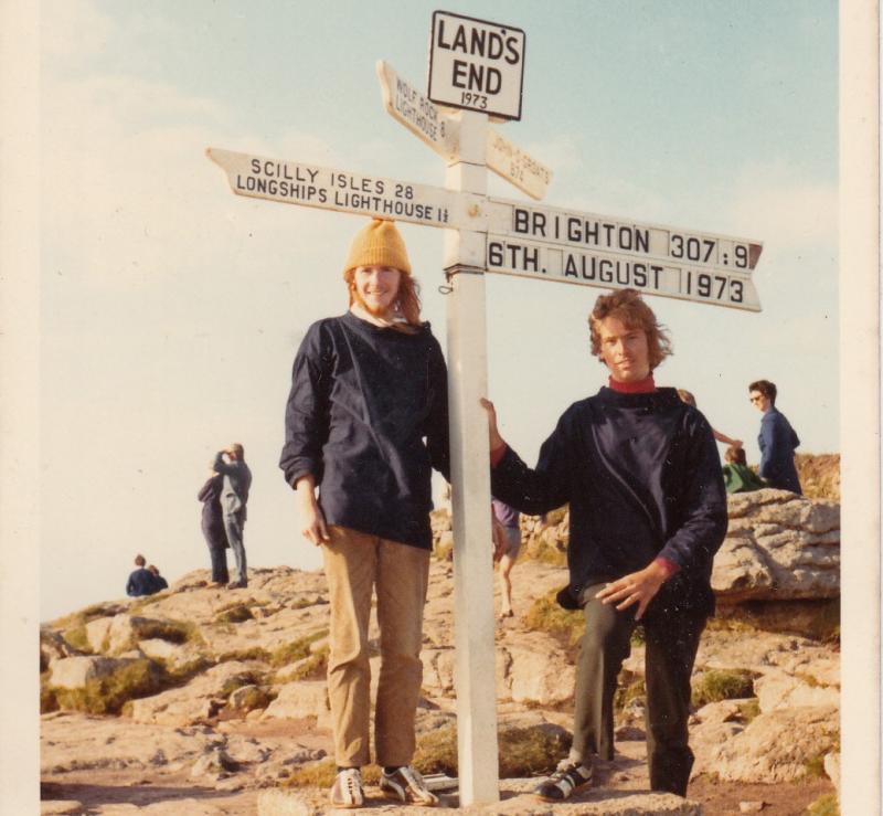 In a scan of an old photo, two men are standing next to the Land's End sign, which points to Brighton and the Scilly Isles. It also has the date 16 August 1973. They are both wearing sweaters and trousers.