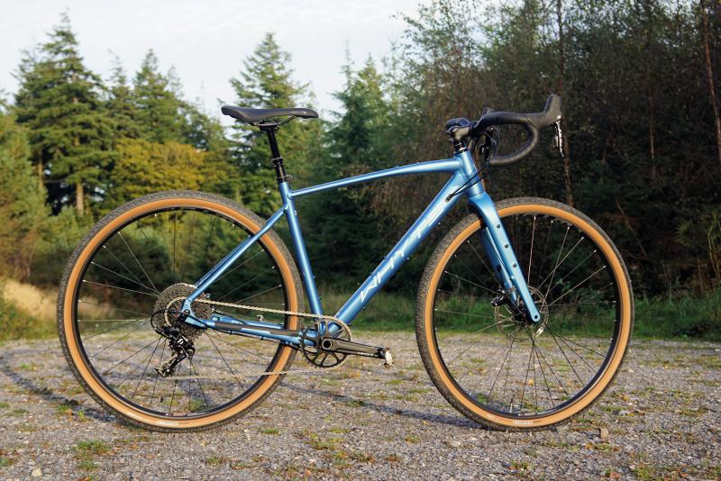 A metallic blue gravel bike propped up on an off-road gravel track