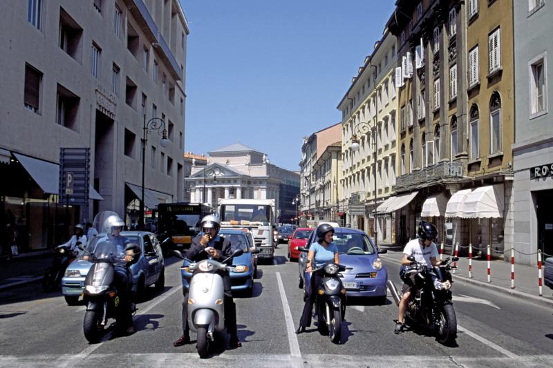 Four lanes of mopeds and cars on a busy urban road in Italy