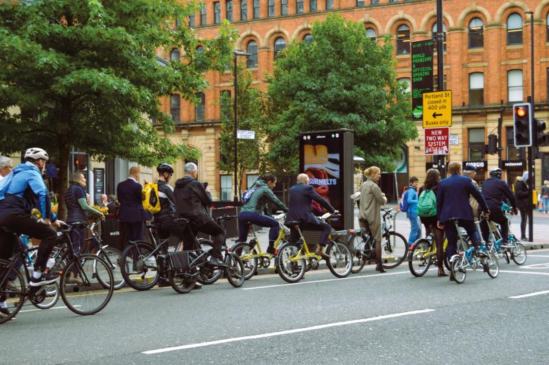 A group of people are cycling along an urban road on a mix of bikes including folding ones