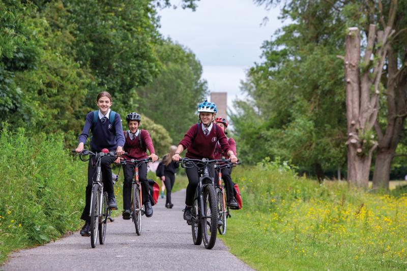 A group of schoolchildren are cycling along a cycle path through a park
